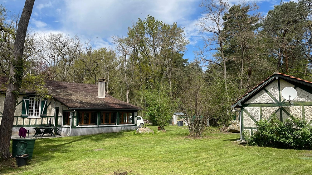 Global outdoor view on the terrain from the back. On the left side, there is a terrace with a green table and 6 chairs, on the right side, there is the apartment.