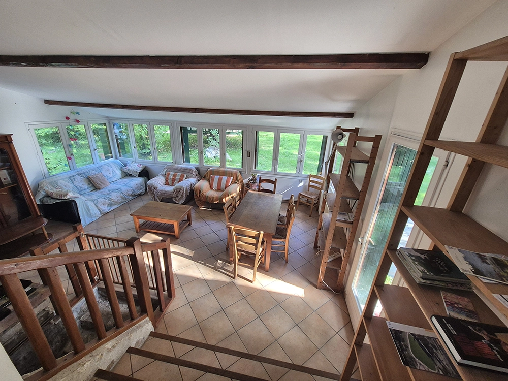Indoor view of the living room with sofa on the left, furniture, wooden table with six chairs and shelves.